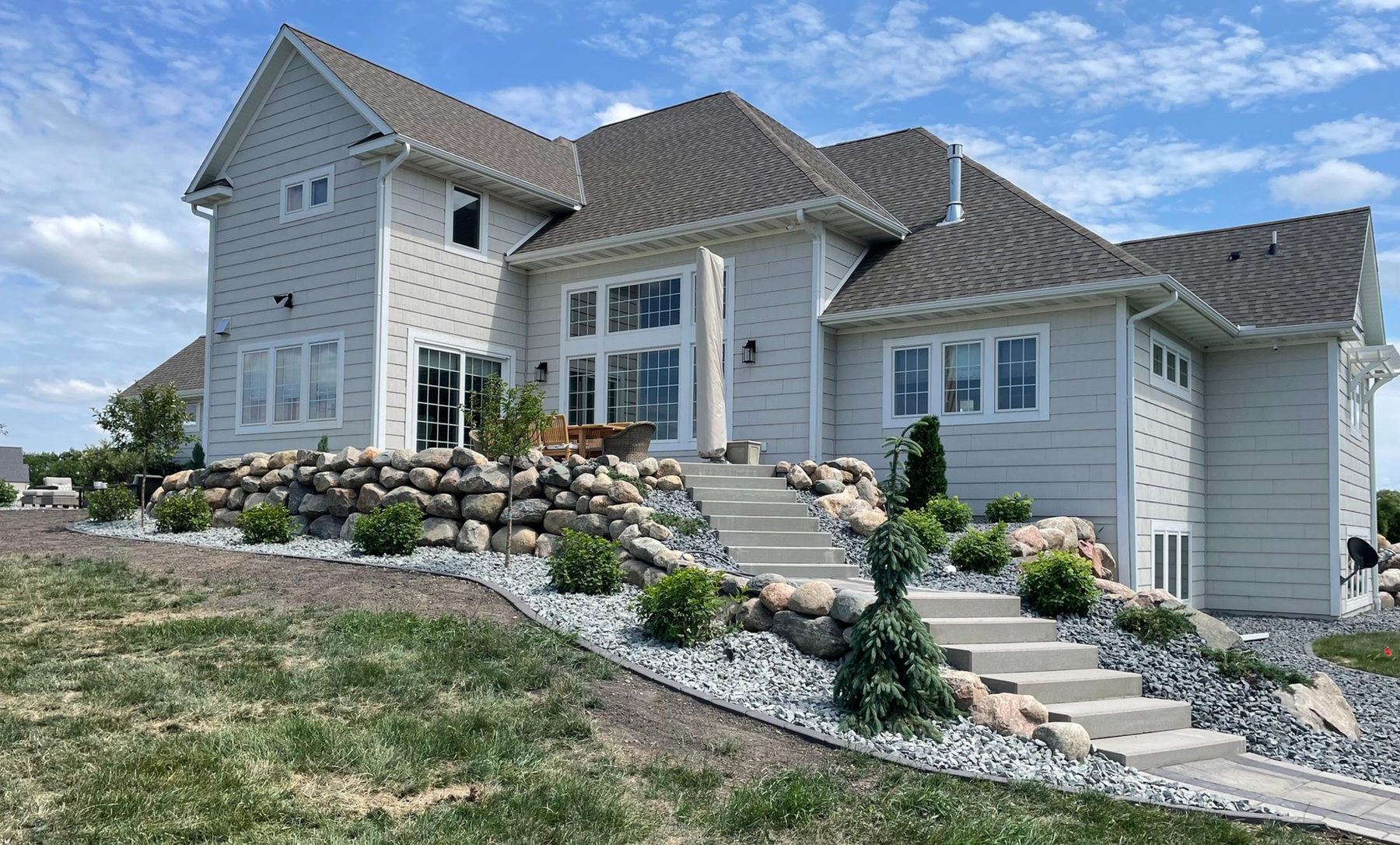 Boulder retaining wall and stone steps leading up to a two-story home, installed by Mankato Landscapers