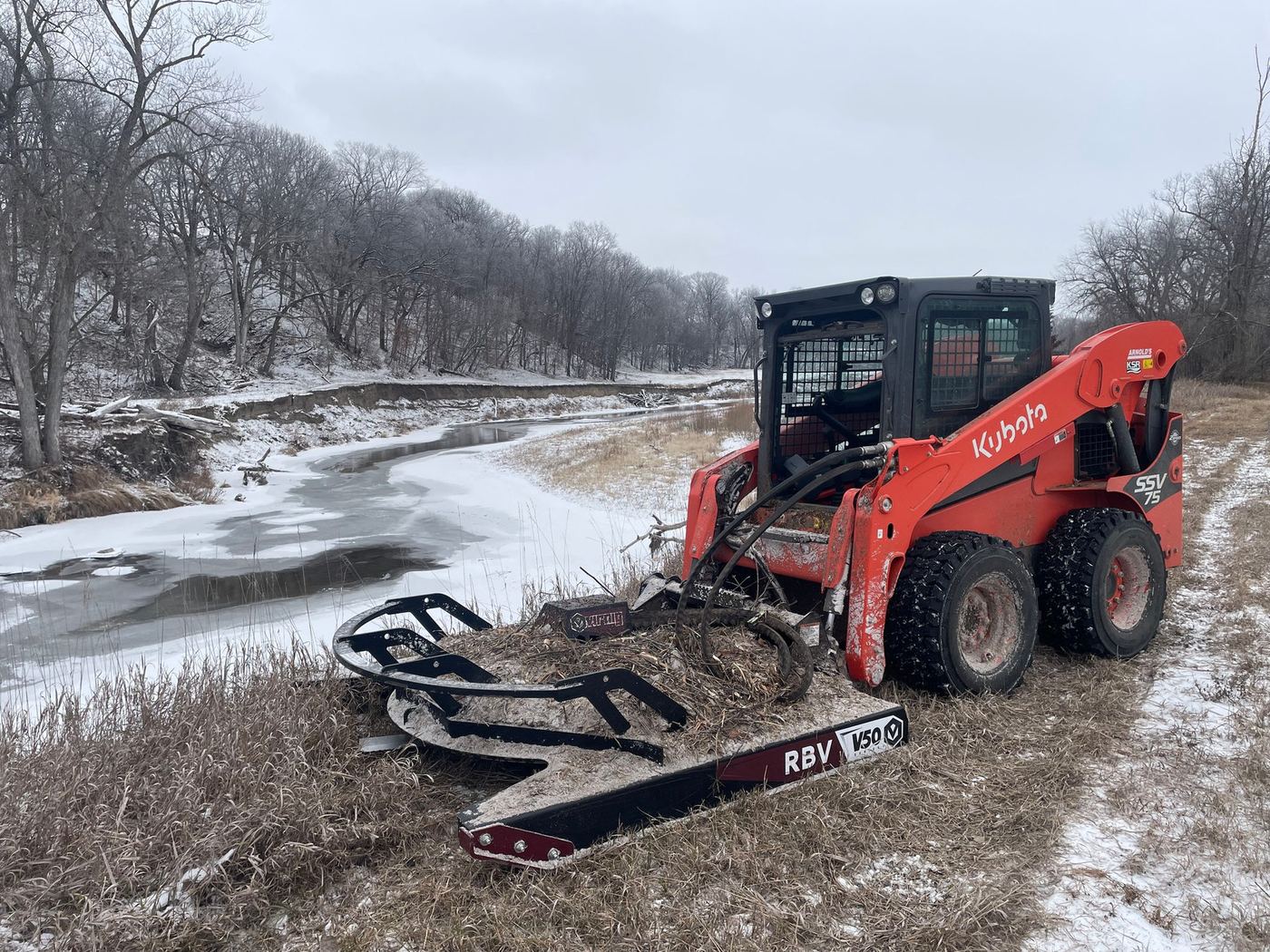 Skid loader with a brush cutter clearing a snowy lot