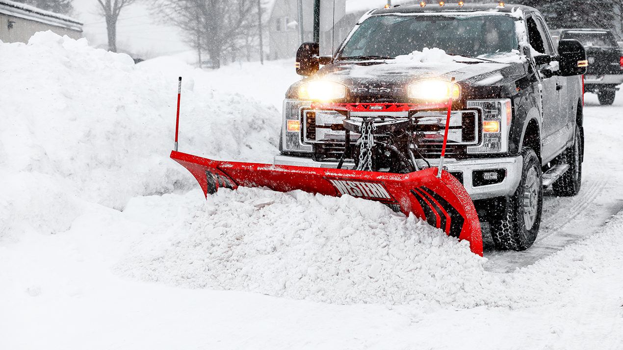 Pickup truck with a red snowplow clearing a snowy lot