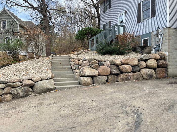 Boulder retaining wall with concrete steps up to a front entry